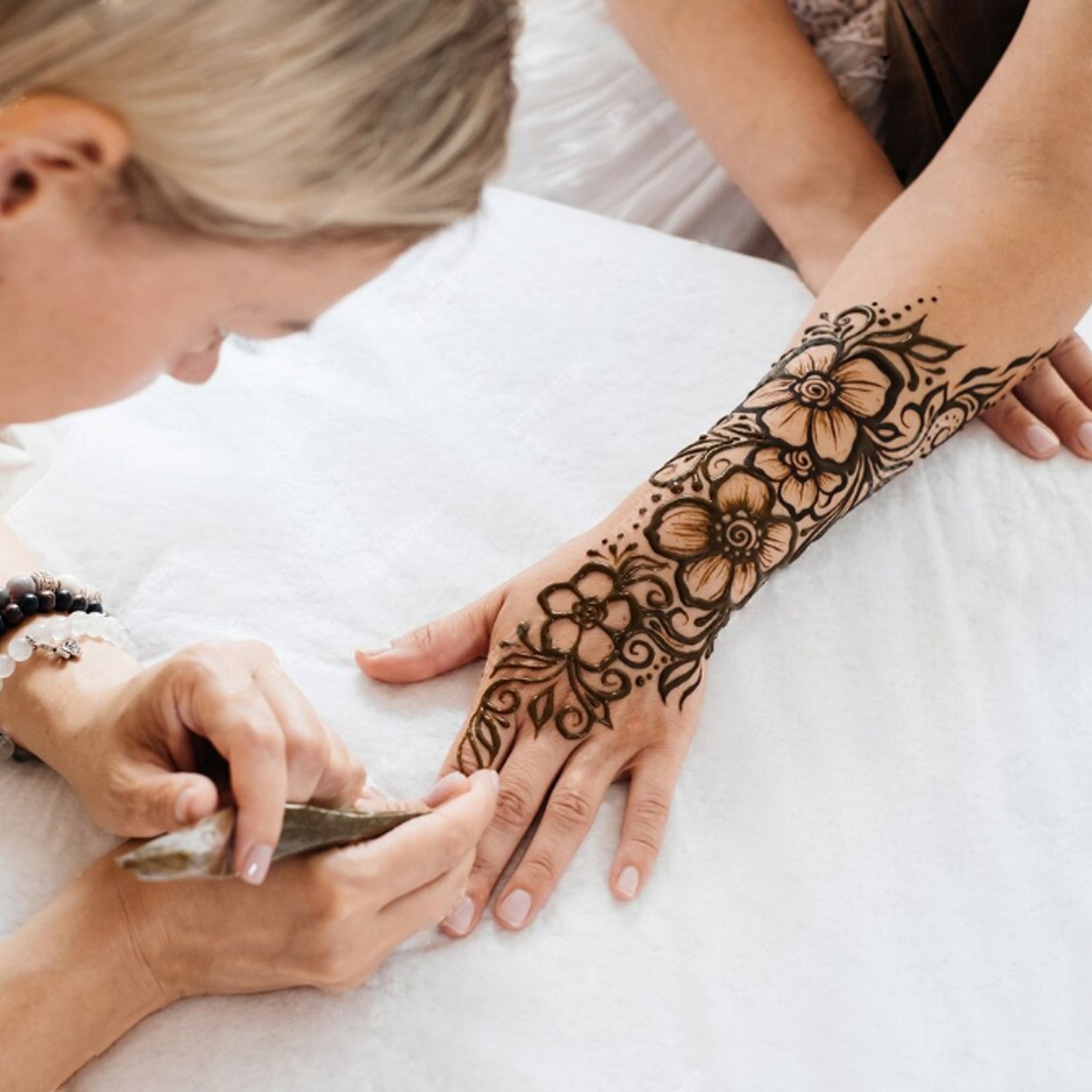 Professional henna artist applying a large, intricate floral Mehndi design on a forearm using Freegrin natural henna paste